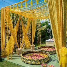 an outdoor ceremony with yellow drapes and flower petals on the ground, surrounded by greenery