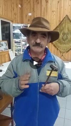 an older man wearing a hat and blue jacket holding a pair of scissors in his hands