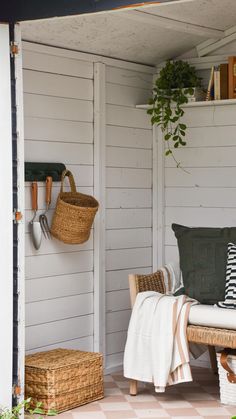 an outdoor room with white walls and wooden furniture, including wicker baskets hanging on the wall