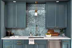 a kitchen with blue cabinets and white counter tops, gold accents on the backsplash