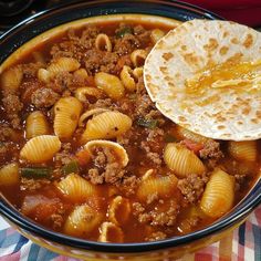 a bowl filled with pasta and meat soup next to a tortilla