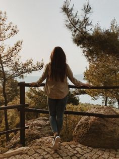 a woman standing on top of a wooden fence next to a tree filled hillside with lots of trees