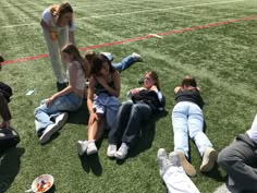 several people are sitting on the grass and one person is taking a photo with her cell phone