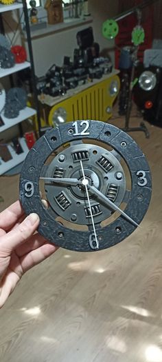 a person holding up a metal clock on top of a wooden table in a shop