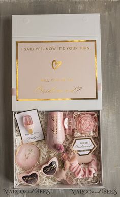 an open gift box containing pink and gold items, including soaps, perfume bottles, and more