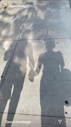 the shadow of two people holding hands on a sidewalk next to a tree and building