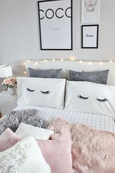 a white bed topped with lots of pillows next to a night stand and pictures on the wall