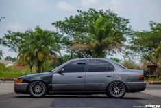 a grey car is parked on the side of the road in front of some trees