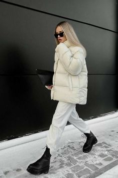 a woman in white is walking down the street wearing black boots and a puffy coat