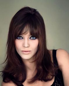 a woman with long brown hair and blue eyes posing for a photo in front of a wall