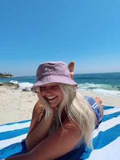 a blonde woman laying on top of a blue and white striped towel next to the ocean