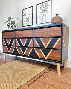 a black and wood dresser with geometric designs on it's drawers, next to a potted plant