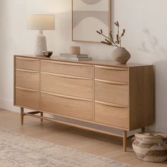 a wooden dresser sitting in a living room next to a lamp and pictures on the wall