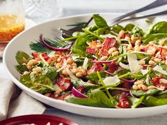 a salad with spinach, bacon and cheese in a white bowl on a table