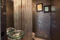 a bathroom with a glass sink next to a toilet and shower curtain in the corner