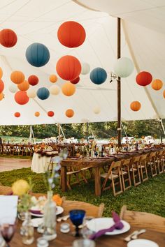 an outdoor tent with tables, chairs and paper lanterns hanging from the ceiling