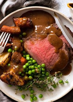 a white plate topped with meat, peas and potatoes next to a fork on top of a table