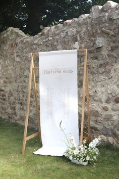 a white sign sitting on top of a grass covered field next to a stone wall