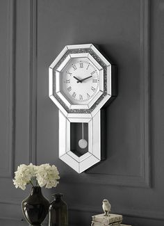 a white clock mounted to the side of a wall next to a vase with flowers