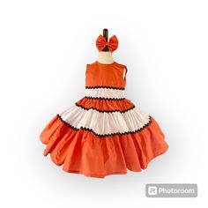 an orange and white dress with a red bow on the headband is hanging in front of a white background