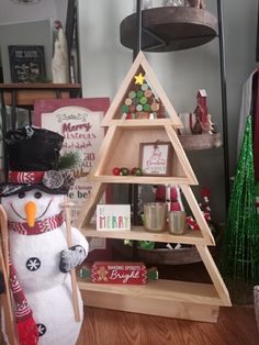 a wooden christmas tree with a snowman on top and other holiday decorations in the background