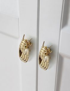 a pair of gold bee earrings sitting on top of a white cabinet door next to each other