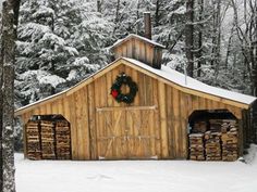 a barn with a wreath on the door and snow covered trees in the back ground