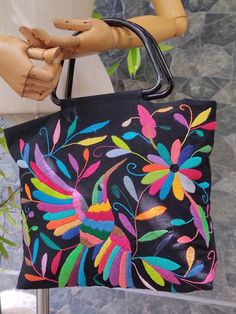 a wooden mannequin holding a black bag with colorful flowers on it