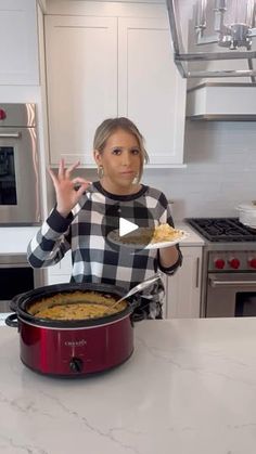 a woman standing in front of a red crock pot filled with macaroni and cheese