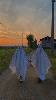 two people in white cloths walking down a dirt road at sunset with one holding the other's hand