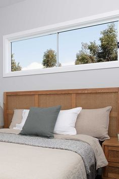 a bed with two windows above it and pillows on the headboard, in front of a window