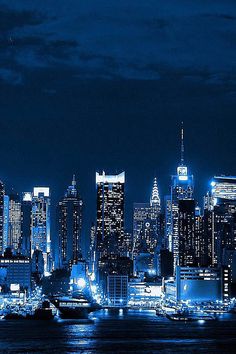 the city skyline is lit up at night, with boats in the water below it