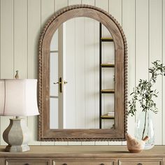 a mirror sitting on top of a wooden dresser next to a lamp and potted plant