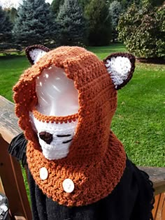 a person wearing a knitted animal mask on top of a wooden bench in a park