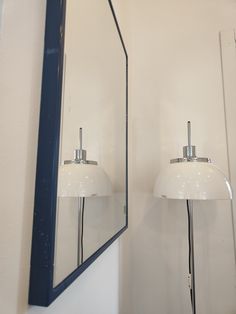 a bathroom mirror sitting next to a wall mounted light on top of a white wall