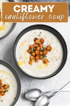 two bowls of creamy cauliflower soup with garnish on top and spoons to the side