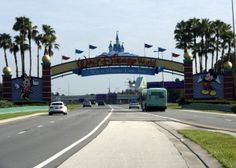 the entrance to disney world with cars driving under it and palm trees in the background