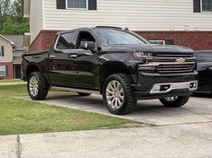 a black truck is parked in front of a house with two other trucks behind it