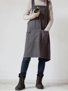 a woman wearing an apron and holding a bottle in one hand while standing against a white wall