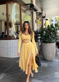 a woman in a yellow dress is walking down the street with her hand on her hip