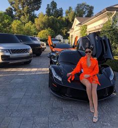 a woman in an orange dress sitting on top of a black sports car