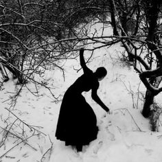 a woman standing in the snow next to trees