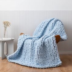 a blue knitted blanket sitting on top of a wooden chair next to a white table