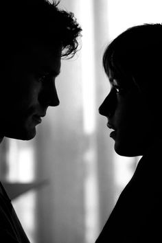 a man and woman are facing each other in black and white, with light coming through the window behind them