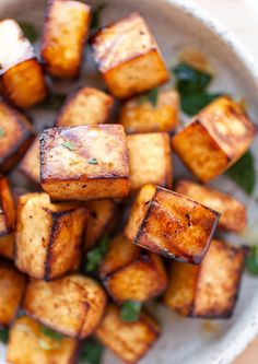 a white bowl filled with cubed tofu and garnished with green leaves