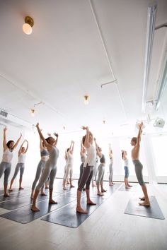 a group of people standing in a room with their arms up and one person doing yoga