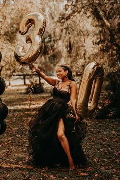 a woman in a black dress is holding balloons and posing for the camera with her number 3 balloon