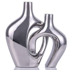 two silver vases sitting next to each other on a white surface, one is shaped like an abstract figure