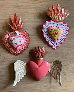 three heart shaped ornaments on a table with angel wings and a pink heart in the middle