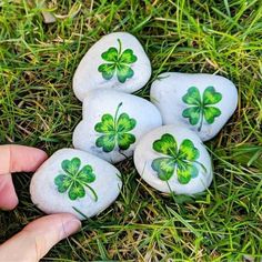 four green shamrocks painted on rocks in the grass with one hand pointing at them